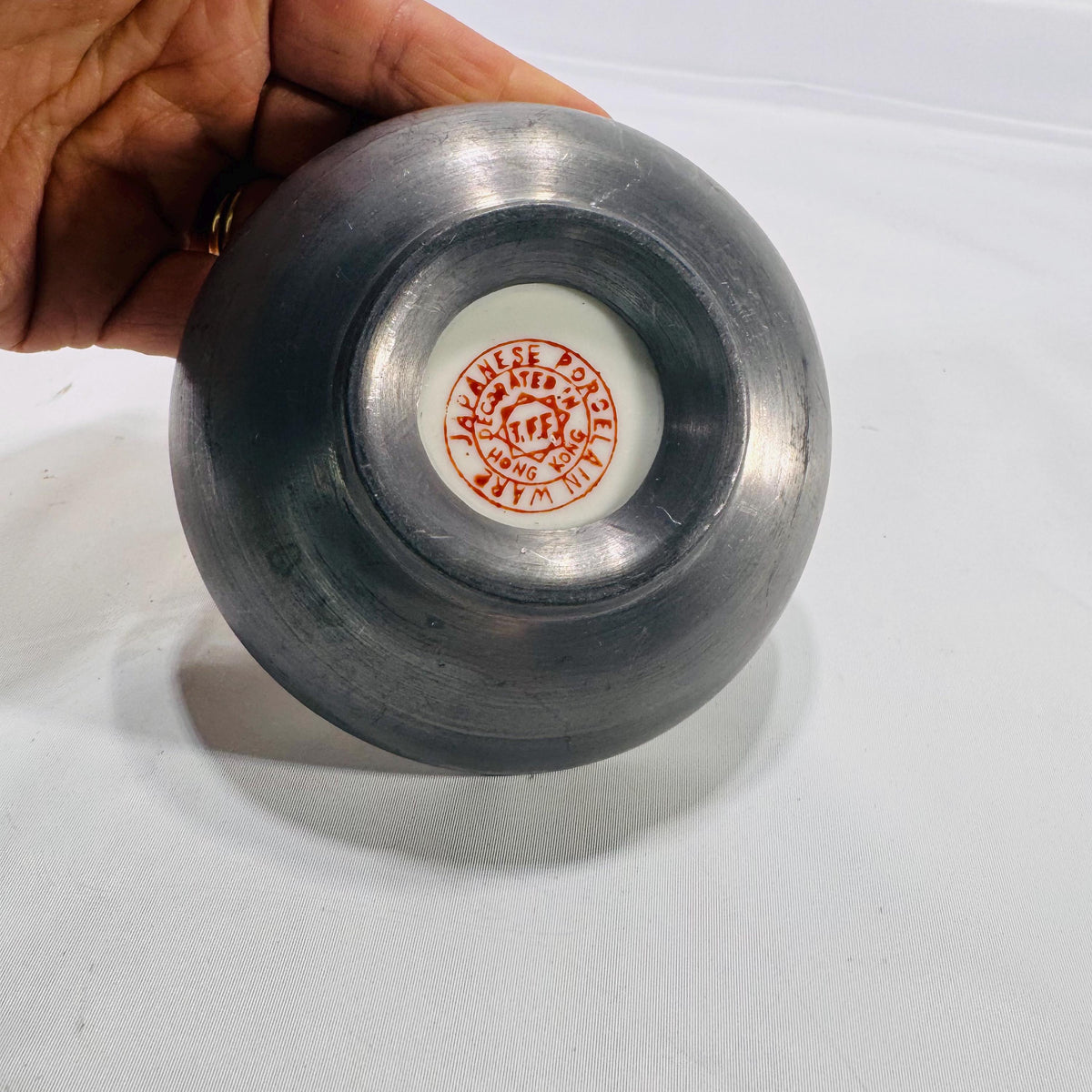 Underside of cloisonné bowl with a white circular porcelain insert stamped “Chinese Porcelain Inlaid in Hong Kong,” set into a dark metal base.