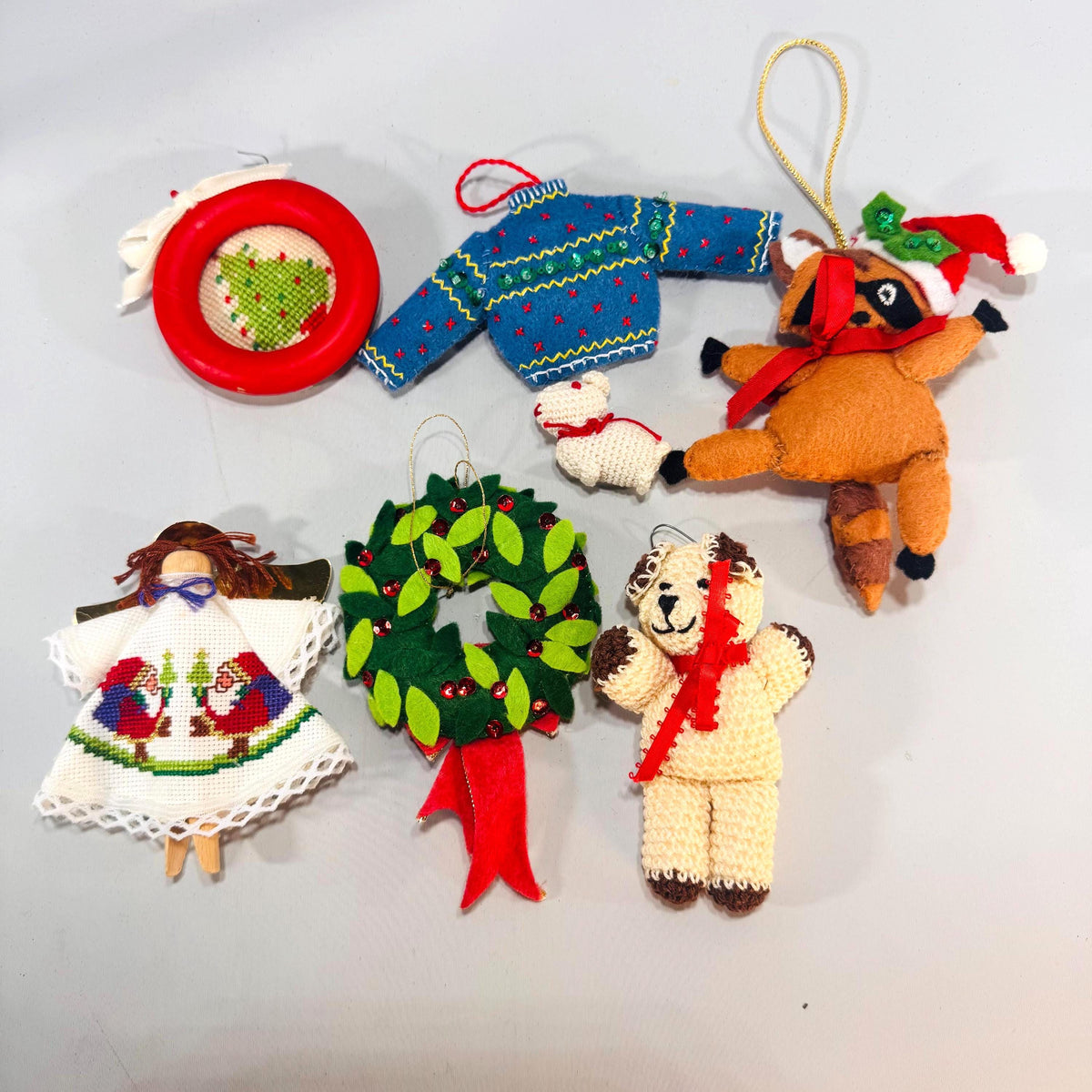 Set of seven handmade vintage Christmas ornaments—felt wreath, raccoon, sweater, clothespin angel, crochet bear and lamb, red needlepoint hoop.