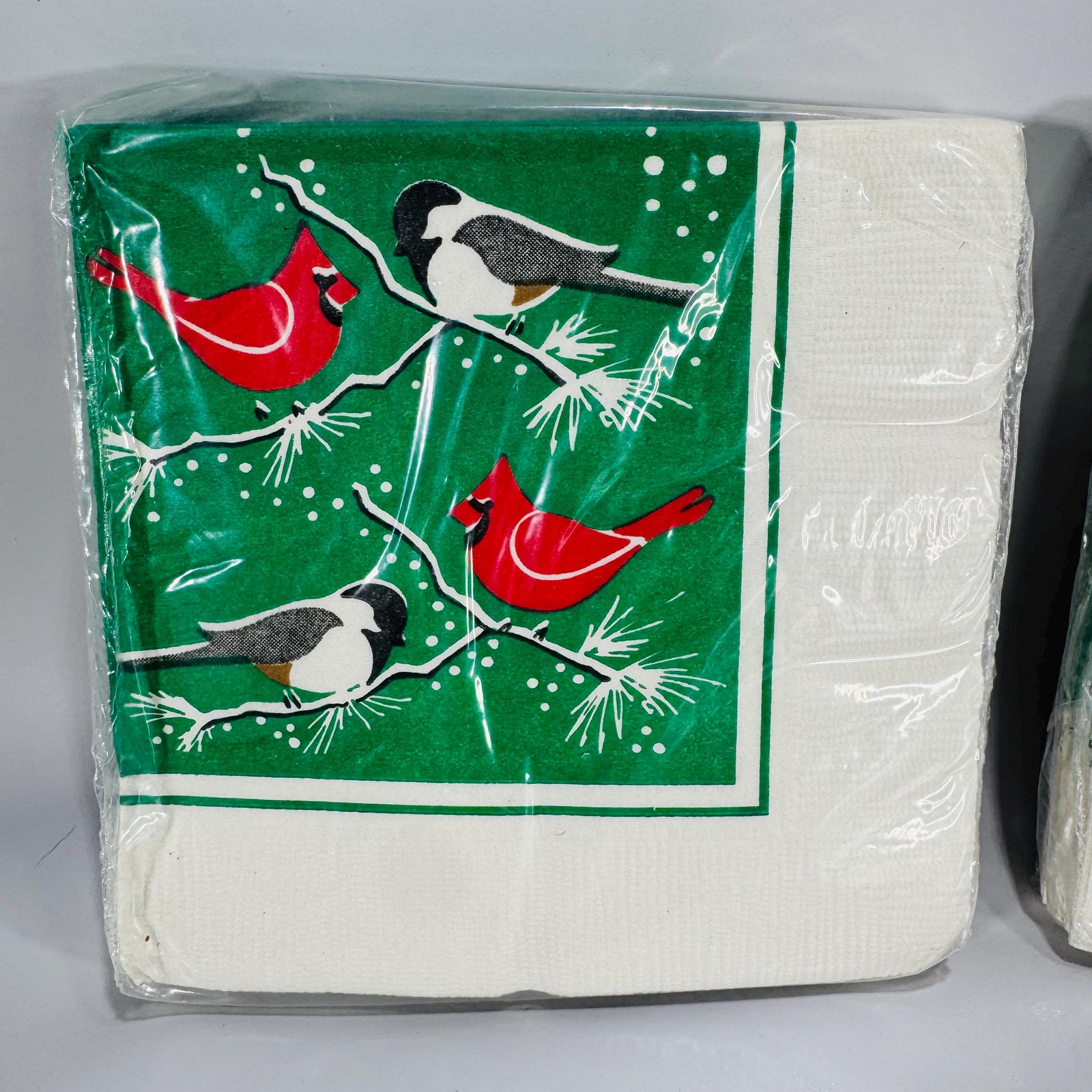 Two packs of vintage Wild Birds Unlimited Christmas napkins featuring red cardinals and chickadees on green pine branches with snowflakes.