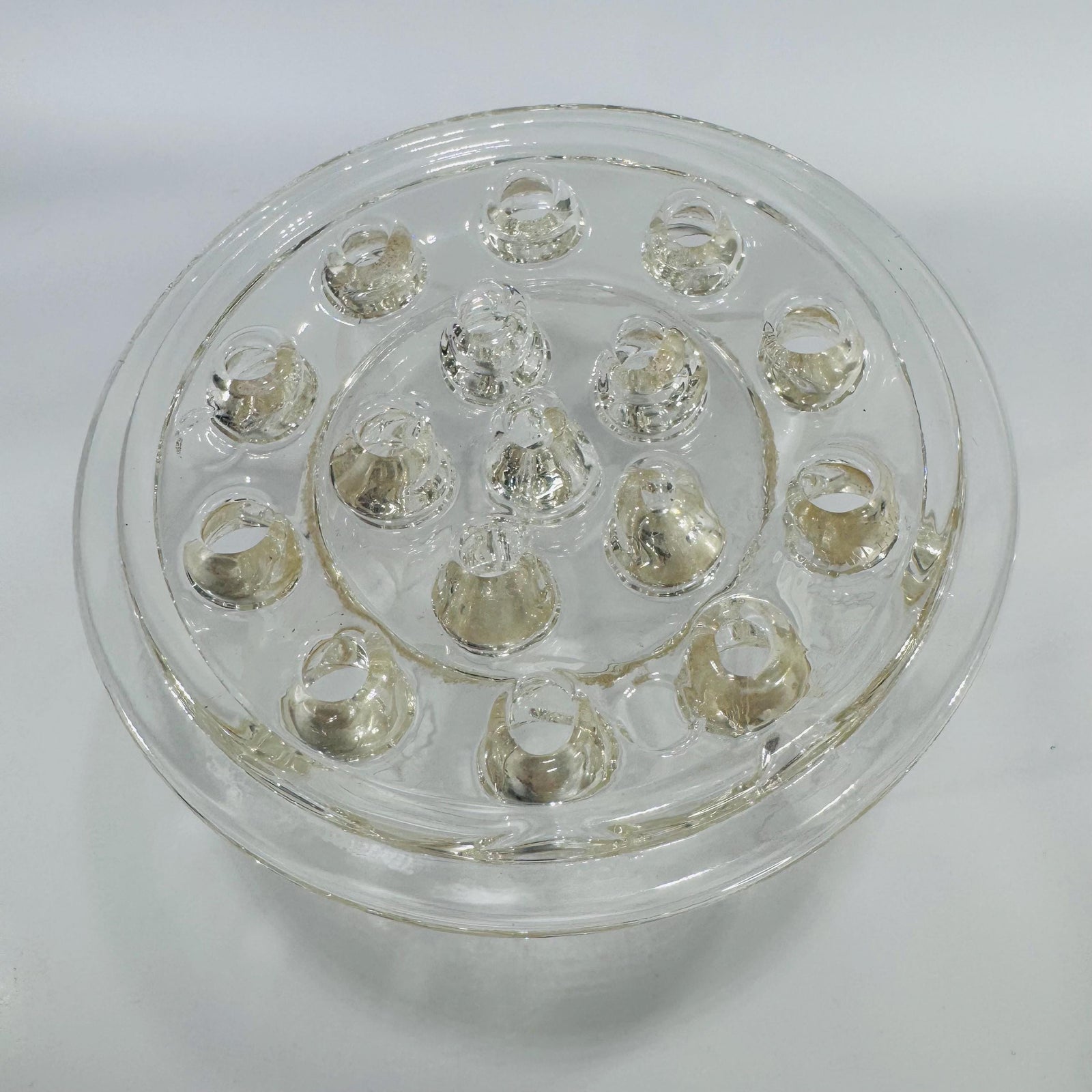 Clear round glass flower frog with multiple stem holes in a dome design, viewed from above