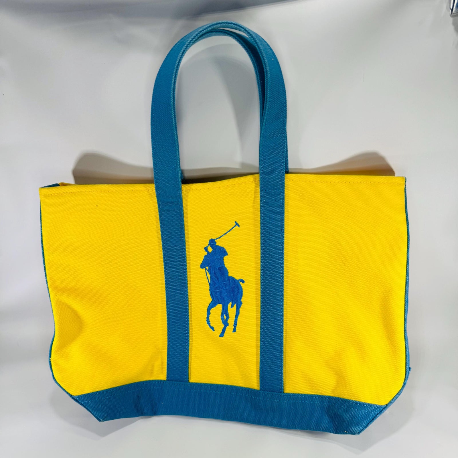 Bright yellow Ralph Lauren canvas tote with teal straps and oversized blue Big Pony logo, front view against light background.
