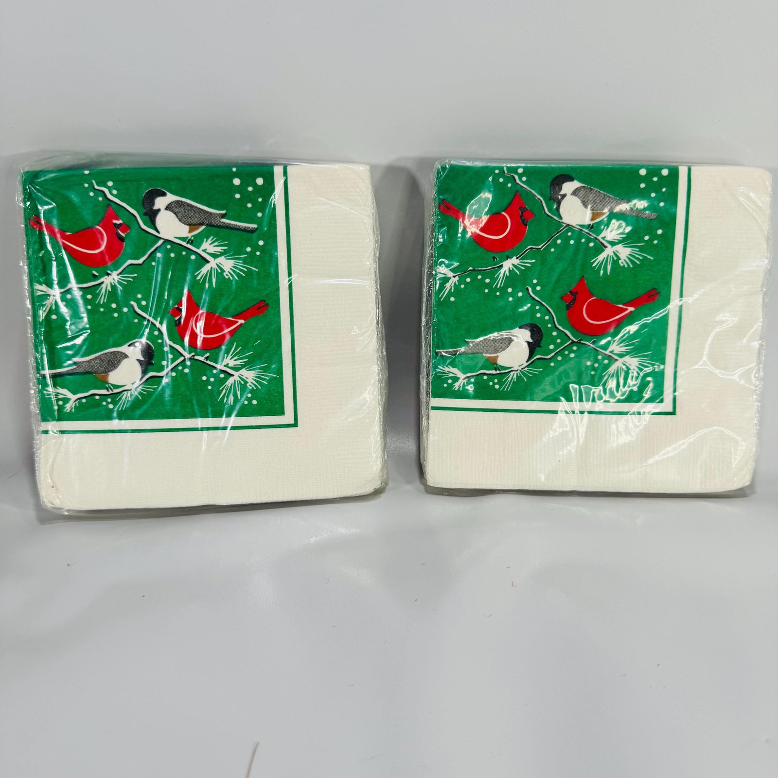 Two packs of vintage Wild Birds Unlimited Christmas napkins featuring red cardinals and chickadees on green pine branches with snowflakes.