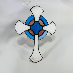 Front view of stained-glass Celtic cross with blue ring and white arms, hanging by white cord on a white background.