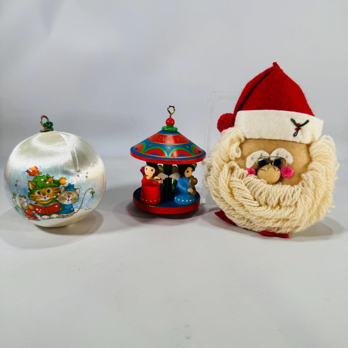 Trio of vintage ornaments—satin cat ball, wood angel carousel, and plush yarn Santa.