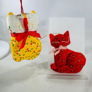 Two 1970s–80s handmade fabric cat ornaments, one yellow and one red, with floral prints and ribbon bows.