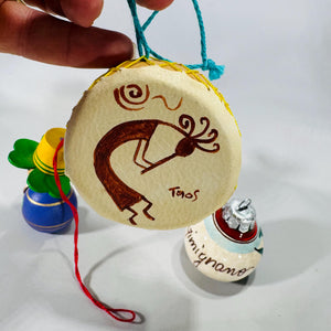 Set of four vintage travel-themed Christmas ornaments including a wood clown, wooden doll with pfennig coin, Taos drum, and hand-painted poppy ornament.