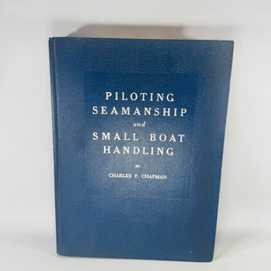 Navy blue hardcover vintage boating manual titled “Piloting, Seamanship and Small Boat Handling” by Charles F. Chapman, with interior photos of nautical charts and seamanship spreads.