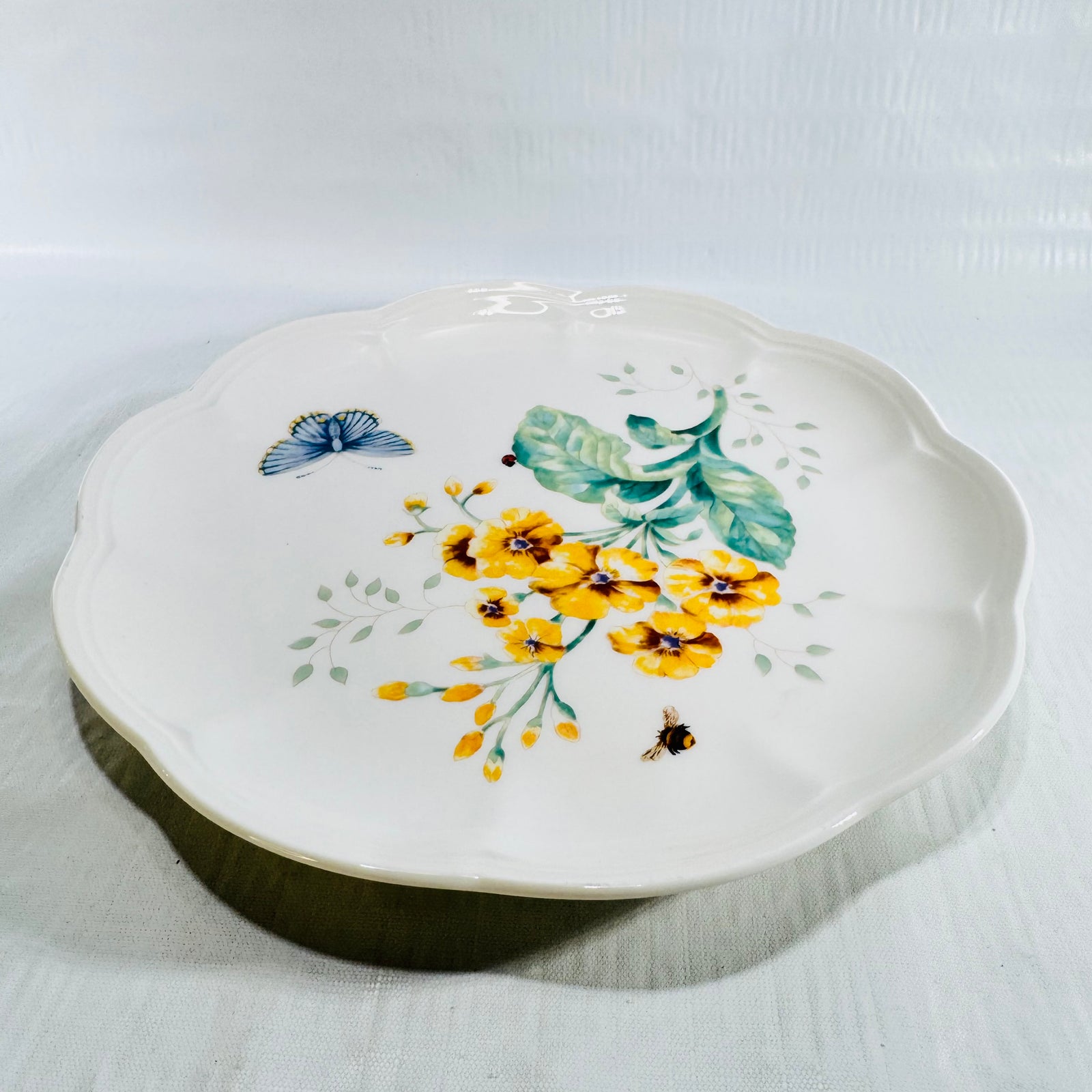 Angled view of Lenox Butterfly Meadow Fritillary 9 inch plate with yellow flowers and blue butterfly