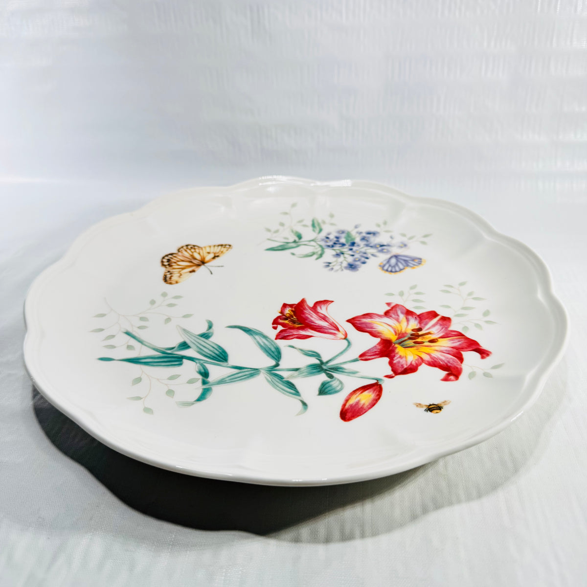 Angled view of the Lenox Butterfly Meadow Fritillary 11 inch dinner plate with red lily