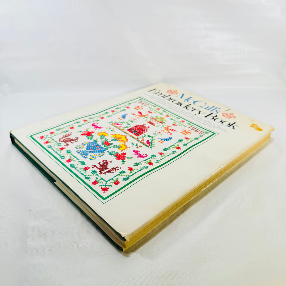 McCall's Embroidery Book angled view showing jacket wear and toned page edges