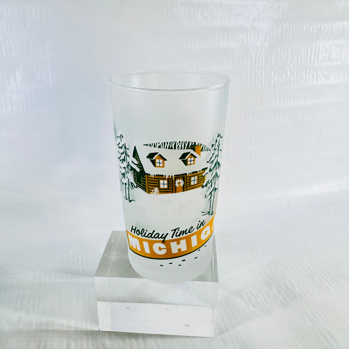 Frosted glass tumbler with a snowy log cabin, pine trees, and the Holiday Time in Michigan banner on the front.