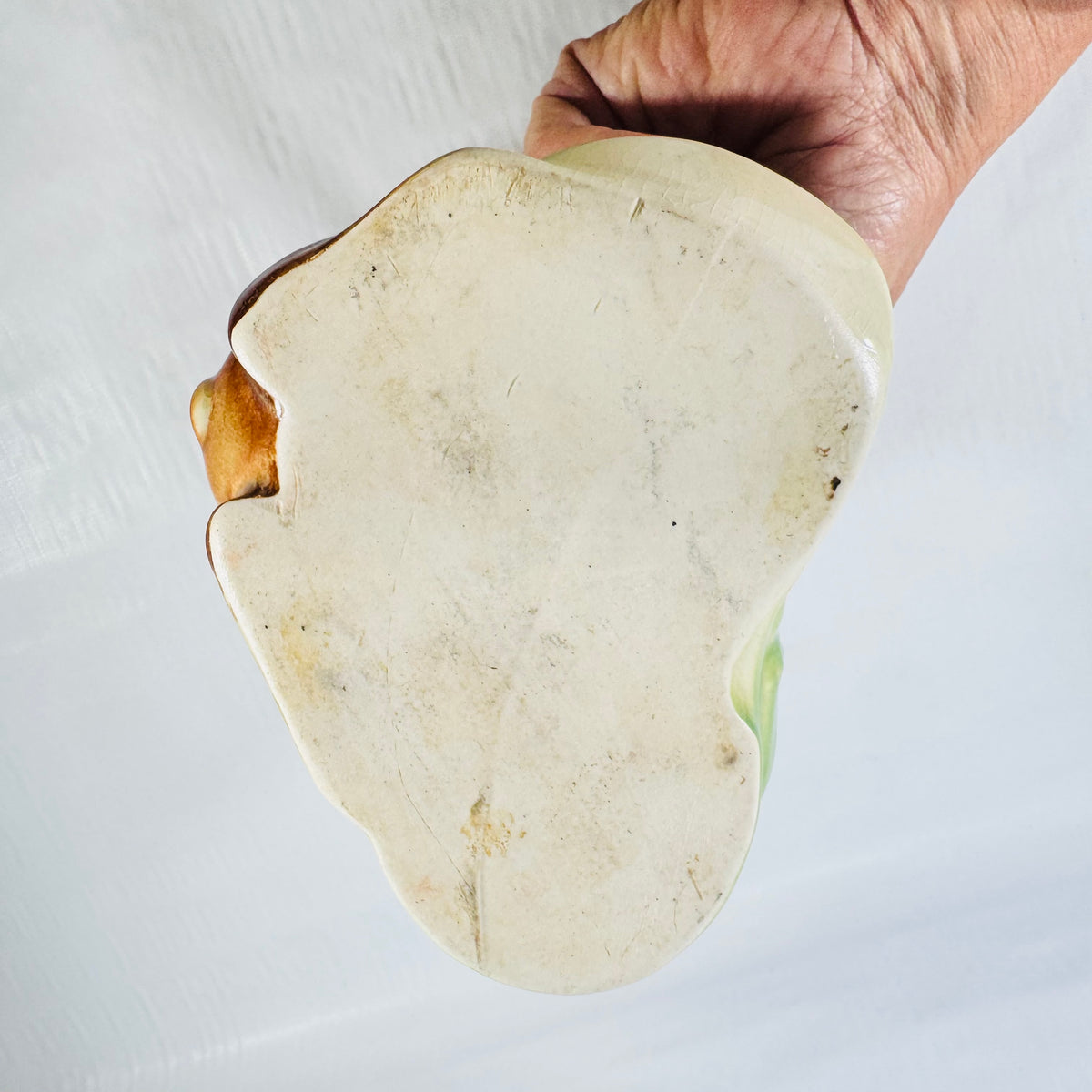 Unglazed base of the puppy planter held in a hand, showing surface grime and spots.