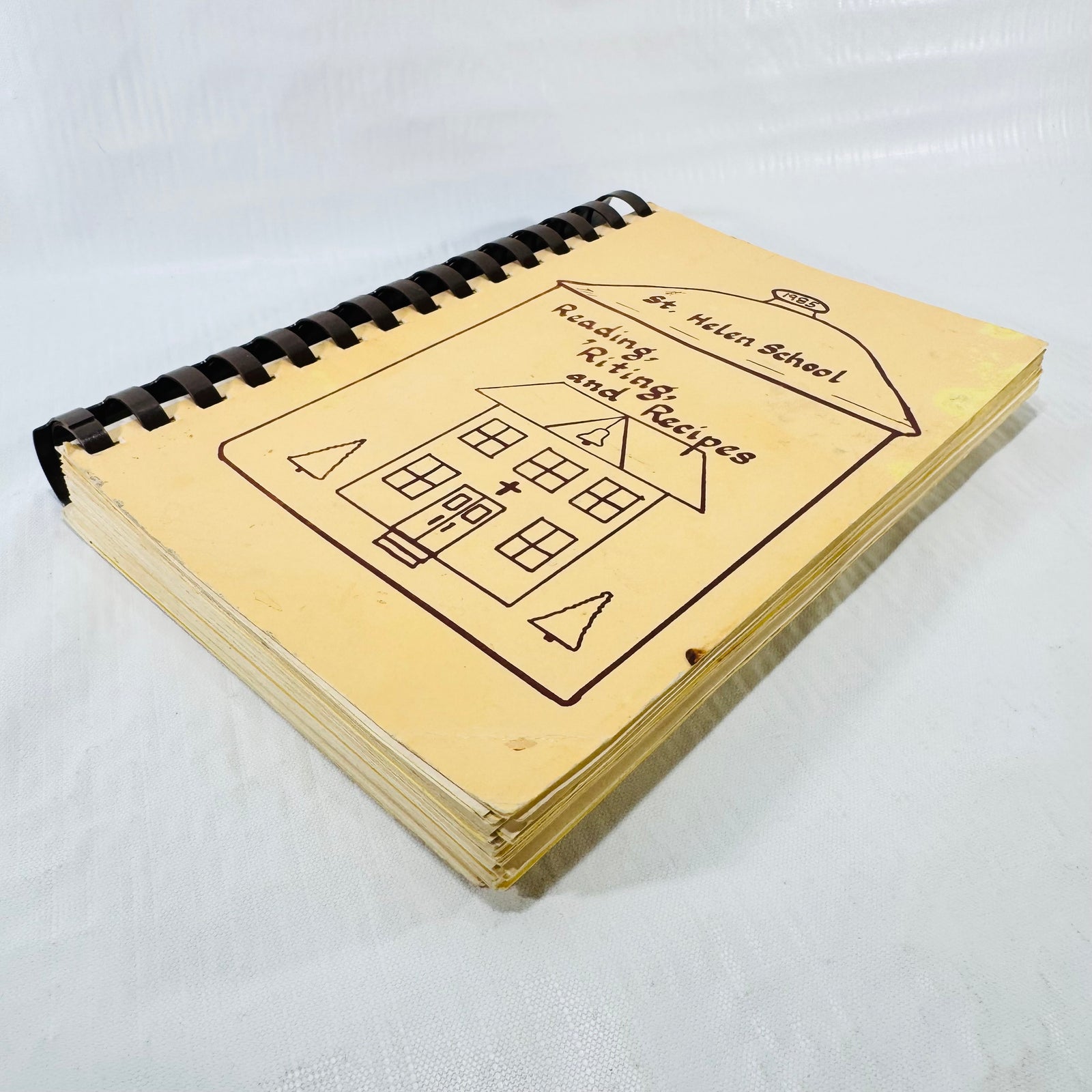 Angled view of the St. Helen School cookbook showing cover wear and comb spine