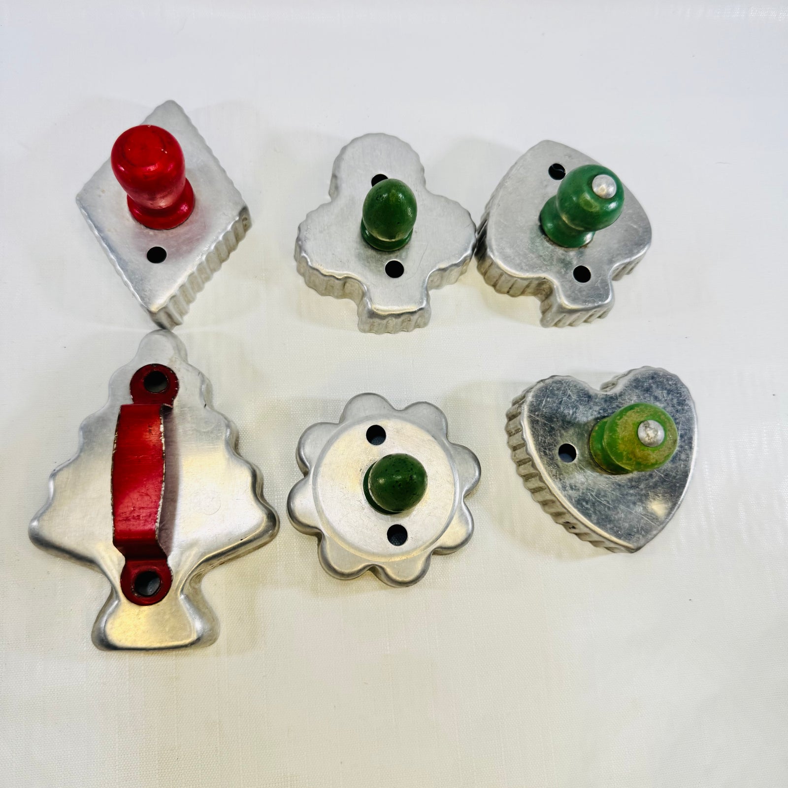 Six vintage aluminum cookie cutters with red and green wood handles: bridge suits, Christmas tree, and rosette