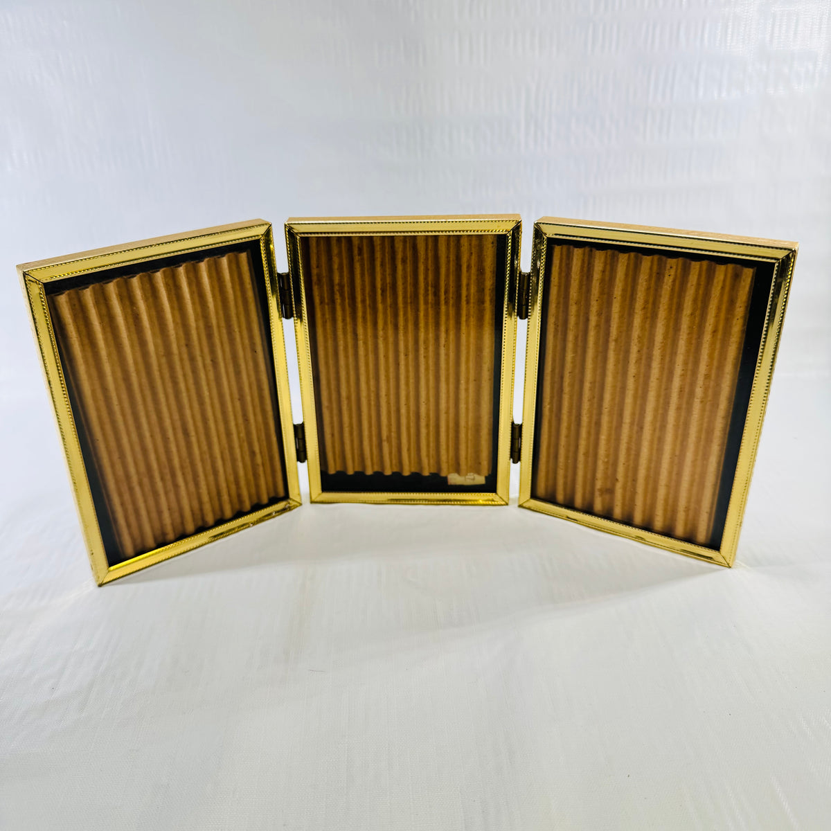 Vintage gold tone tri-fold hinged picture frame standing open, three 4x5 panels with ribbed inserts