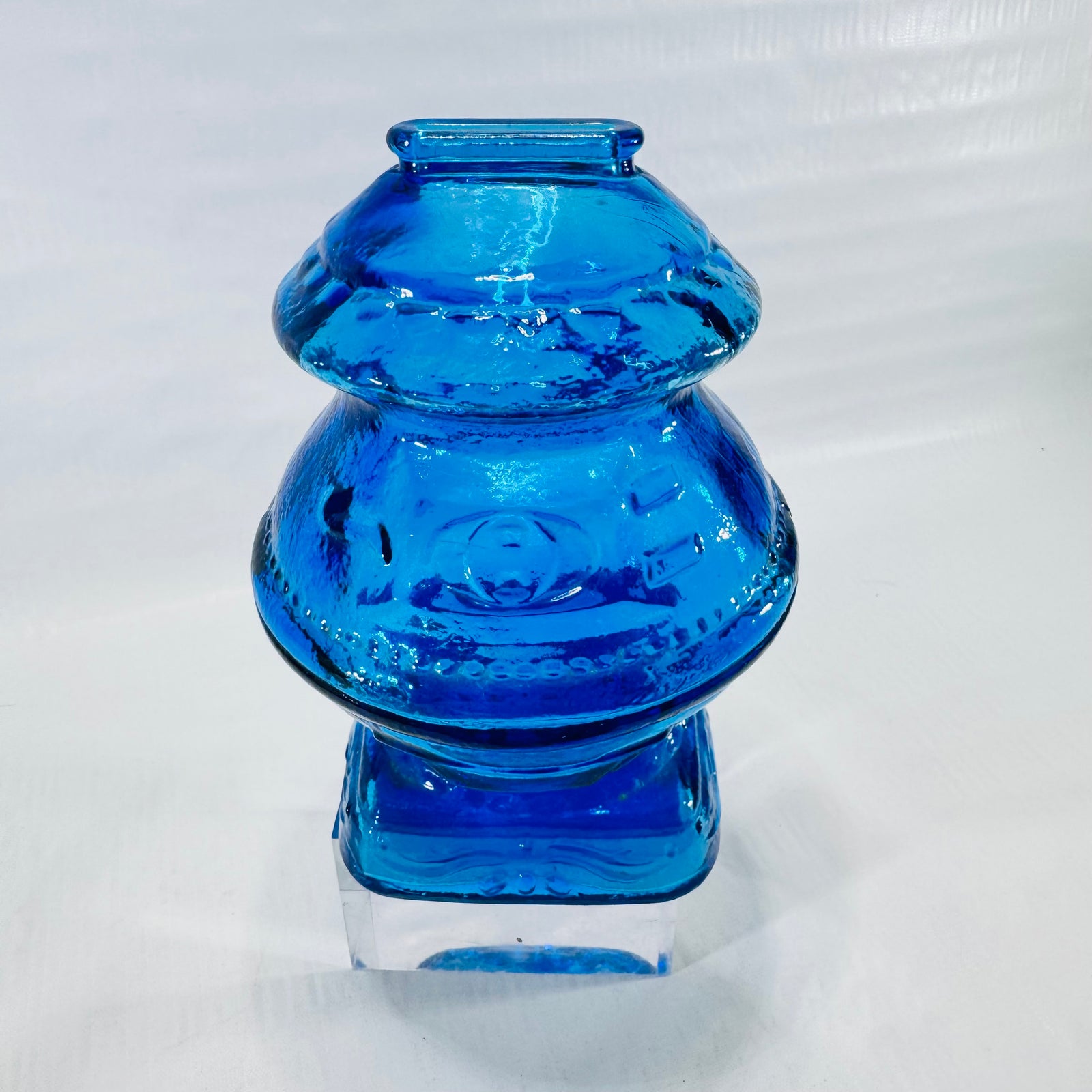Front of a Wheaton blue glass gumball machine coin bank with an embossed round medallion and square base.