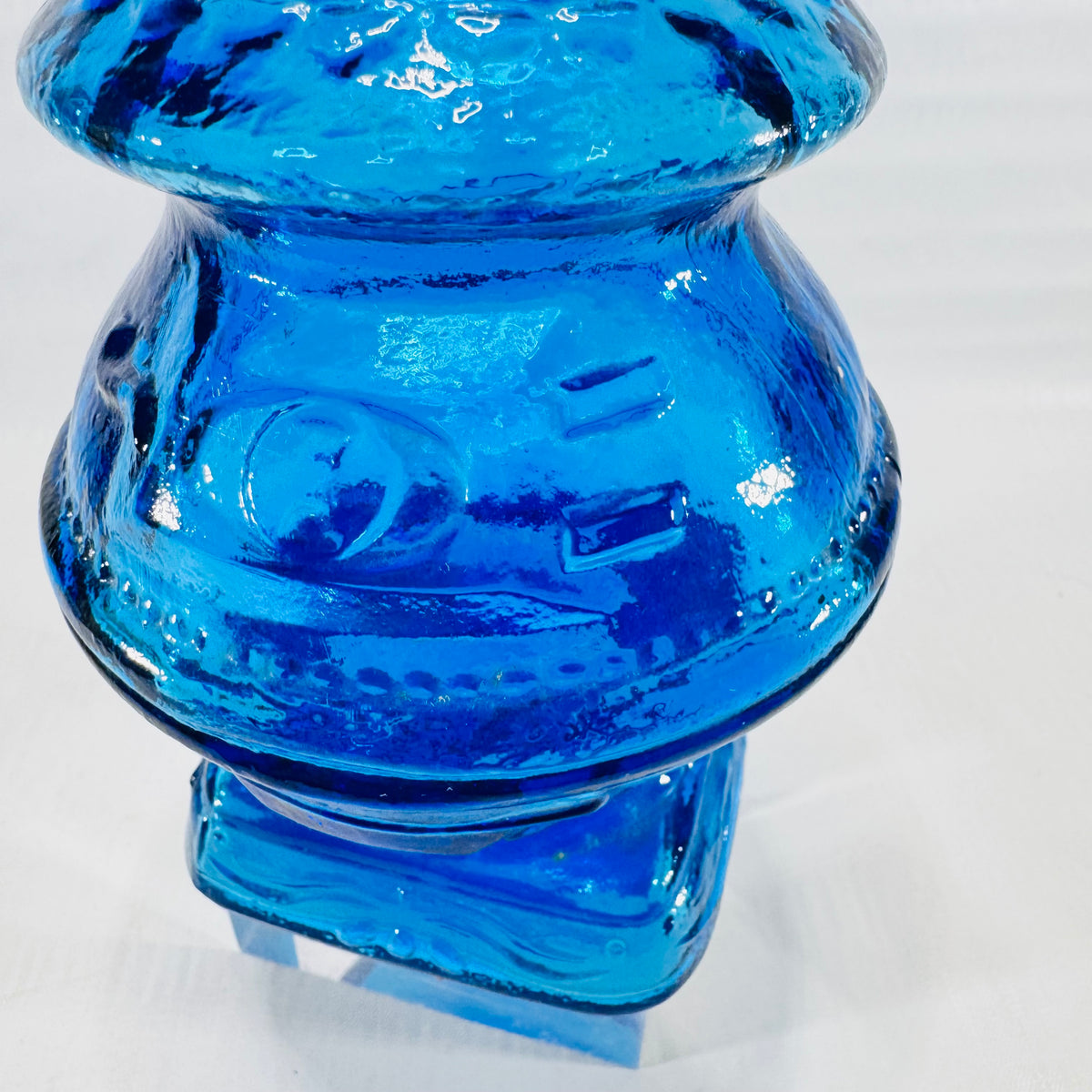 Close side view of the blue glass gumball machine bank showing embossed panels and beaded bands.